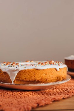 Yuvarlak Paskalya keki, beyaz protein kremi ve mutfaktaki ahşap masaya renkli serpiştirilmiş. Ön görünüm