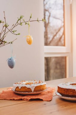 Yuvarlak Paskalya keki, beyaz protein kremi ve mutfaktaki ahşap masaya renkli serpiştirilmiş. Ön görünüm