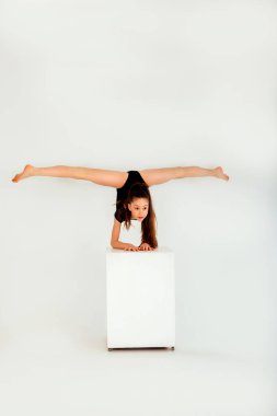 Siyah taytlı bir jimnastikçi kız beyaz arka planda beyaz bir küpte numaralar yapıyor. Ön görünüm
