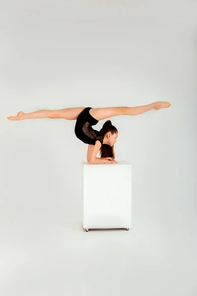 一个穿着黑色紧身衣的女体操运动员在白色背景的白色立方体上做手脚 — 图库照片