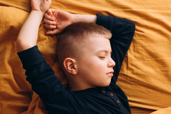 The boy sleeps in the yellow bed in the morning. Close-up portrait of a sleeping boy. View from above