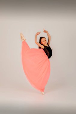 Bale konsepti. Siyah jimnastik mayo giyen, beyaz arka planda, pembe etekli, zarif bir duruşu olan bir kız. Ön görünüm