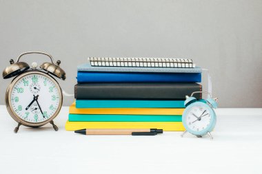 Kırtasiyeli işyeri. Çok renkli not defterleri, gri bir duvara karşı beyaz ahşap bir masada mavi alarm saati. Ön görünüm