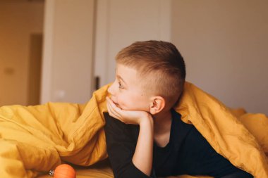 Neşeli bir çocuk sarı battaniyenin altından çıkıyor. Kötü durumdaki çocuk. Ön görünüm