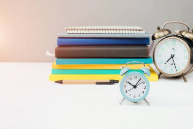 Kırtasiyeli işyeri. Çok renkli not defterleri, gri bir duvara karşı beyaz ahşap bir masada mavi alarm saati. Ön görünüm