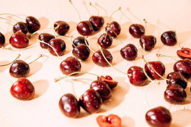 A large cherry with water drops close up on a light orange background in sunlight, selective focus. Top view