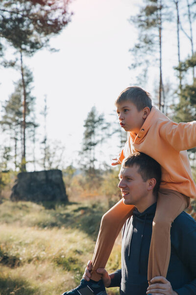 Dad and son on a walk in the forest in sunny weather. Family leisure. The father carries his son on his shoulders. Front view