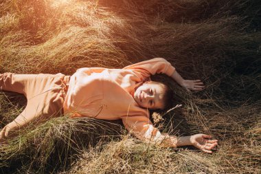 Neşeli bir çocuk çayırdaki uzun otların üzerinde yatıyor. Parkta açık hava eğlencesi. Üst görünüm