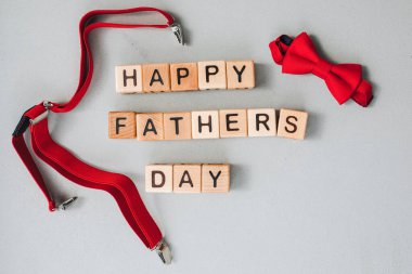 Mutlu Babalar Günü konsepti. Geçmiş, tebrik kartı. Siyah harfli ahşap küpler gri beton bir arka planda, kırmızı erkek aksesuarları, papyon ve pantolon askısı ile serilmiştir. Düz yatıyordu