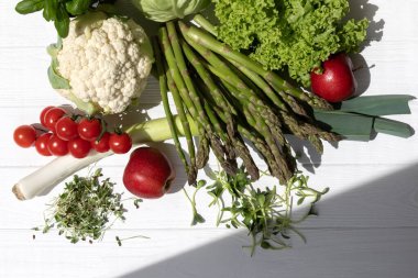 Taze sebzeler, kuşkonmaz, domates, lahana, karnabahar, yeşil salata, bazilika ve elmalar beyaz ahşap arka planda. Düz yatıyordu