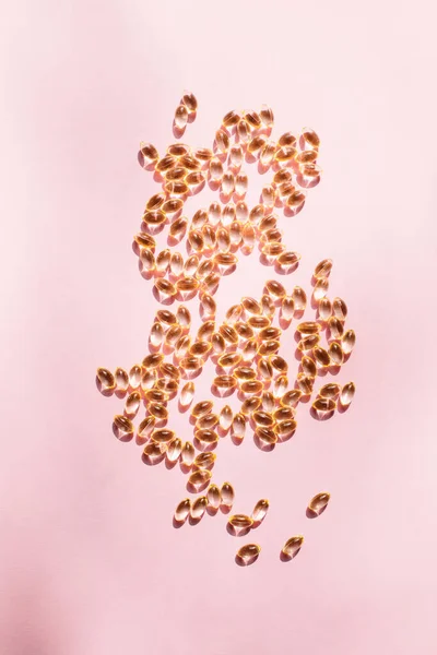 stock image Capsules of vitamins, vitamin d or omega, scattered randomly on a pink background shimmer from sunlight. Flat light