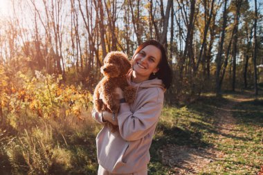 Küçük kahverengi köpeği olan bir kadın parkta yürür. Doğada bir evcil hayvanla vakit geçirmek. Ön görünüm