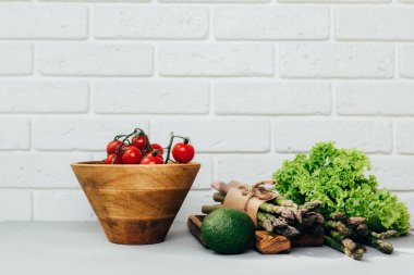 Sağlıklı yemek geçmişi. Taze sebze, ahşap tabakta domates kuşkonmaz, salata, avokado ve beyaz ahşap masada yeşil bazilika. Ön görünüm