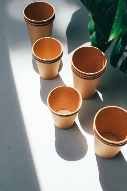 Çevre dostu malzemelerden yemek yemek için tek kullanımlık sofra takımı. Arka planda yeşil yapraklar olan beyaz bir masada kağıt bardaklar. Bozunabilir atık kavramı. Üst görünüm