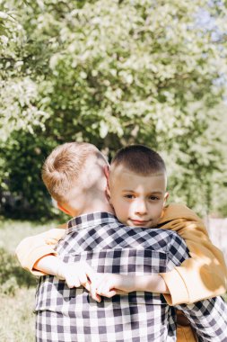 Oğlu güneşli havada babasına sarılıyor. Doğada aile zamanı. Ön görünüm