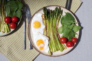 Yeşil kuşkonmaz, taze ıspanak yaprakları, domatesler ve yeşil bir mutfak havlusuyla yeşil bir tabakta çırpılmış yumurta. Sağlıklı yiyecekler. Üst görünüm