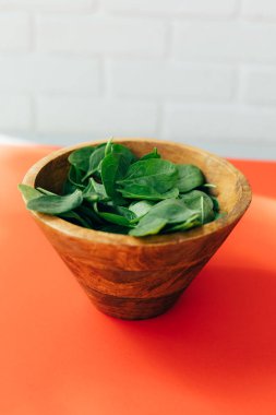 Sağlıklı yemek geçmişi. Yeşil ıspanak, kırmızı arka planda, gün ışığında, ahşap bir tabakta, yakın planda kalır. Ön görünüm