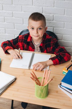 Konsepti okula geri götür. Ders çalışma sürecinde olan bir çocuk kitaplar, defterler ve kalemlerle bir masada oturur. Ön görünüm