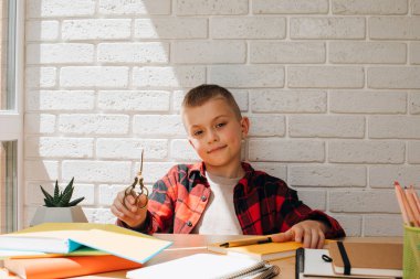 Konsepti okula geri götür. Çalışma sürecinde olan bir çocuk makas, kitap, defter ve kalemlerle bir masada oturur. Ön görünüm