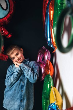 Çocukların doğum günü kutlaması. Neşeli bir çocuk, mavi gömlekli bir öğrenci, renkli balonların arka planında. Ön görünüm