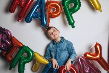 Çocukların doğum günü kutlaması. Neşeli bir çocuk, mavi gömlekli bir öğrenci, renkli balonların arka planında. Ön görünüm