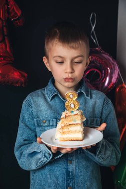Çocukların doğum günü kutlaması. Neşeli bir çocuk, bir parça kek ve sekiz numara şeklinde bir mumla bir okul çocuğu. Çocuk pastadaki mumları üflüyor. Ön görünüm