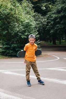 Çocuklar için açık hava aktiviteleri. Halka açık bir parkta kaykaylı kapsül içinde neşeli bir genç çocuk. Beyaz bir okul çocuğu yürüyüşe çıktı. Ön görünüm