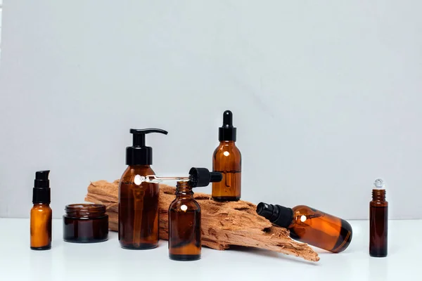 stock image Amber bottles with facial treatment on a wooden stand on a white table. Front view