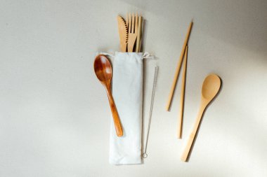 Çatal bıçak takımı. Sıfır atık kavramı, çevre dostu. Yeniden kullanılabilir pipetler, bej beton arka planda keten bir çantada ahşap çatal bıçak takımı. Düz yatıyordu