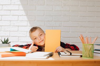 Konsepti okula geri götür. Ders çalışma sürecinde olan bir çocuk kitaplar, defterler ve kalemlerle bir masada oturur. Ön görünüm