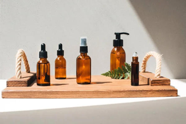 Amber bottles with facial cosmetics, liquid on a wooden tray on the light concrete background. Front view