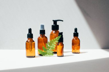 Yüz sıvısı olan kehribar şişeler ve gün ışığı gölgeli açık beton arka plan. Ön görünüm