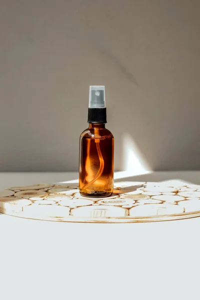 Amber bottle with facial cosmetics, liquid on a wooden tray on the light concrete background. Front view