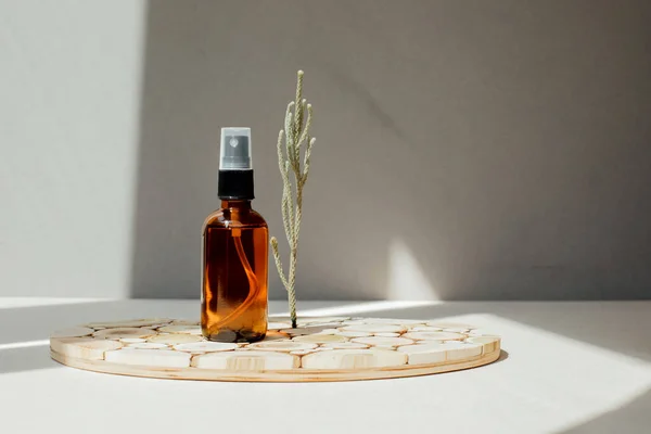 Amber bottle with facial cosmetics, liquid on a wooden tray on the light concrete background. Front view