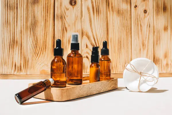 Amber bottles with facial cosmetics, liquid on a wooden tray on the wooden background. Flat lay