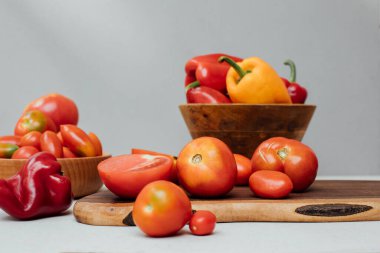 Beton arka planda farklı boyutlarda domates ve dolmalık biber. Bahçe geçmişi, domates ve dolmalık biber hasadı. Olgunlaşmış kırmızı domatesler. Ön görünüm