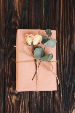 Selamlaşmak için arka plan. Yumuşak pembe kağıda sarılı, koyu ahşap bir arka planda kuru okaliptüs dalı. Üst görünüm