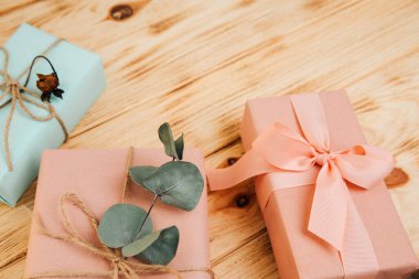 Selamlaşmak için arka plan. Yumuşak pembe ve mavi kağıda sarılı hediyeler, açık ahşap arka planda kuru okaliptüs dallarıyla. Üst görünüm