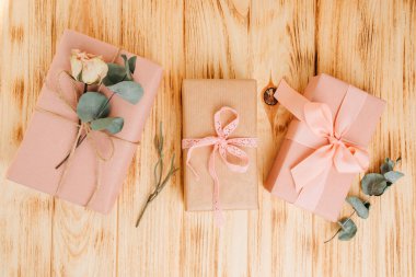 Selamlaşmak için arka plan. Hafif ahşap arka planda kuru okaliptüs dalıyla yumuşak pembe kağıda sarılmış bir hediye. Üst görünüm