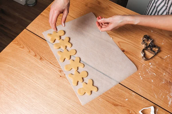 Close up womens hands lay out the formed cookies in the form of a human on a baking sheet on a wooden table in the kitchen. Cooking desserts at home. Top view