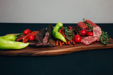 Yeşil kağıt ve domatesli ahşap tepside farklı tip ve boyutlarda sosis. Arka planda tütsülenmiş sosis seti. Ön görünüm