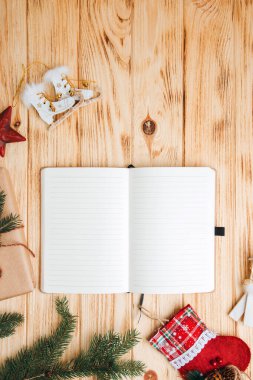 Noel arkaplanı selamlama içindir. Yeşil kozalaklı ağaç dalları, Noel oyuncakları ve açık ahşap bir arka planda açık bir defter. Üst görünüm