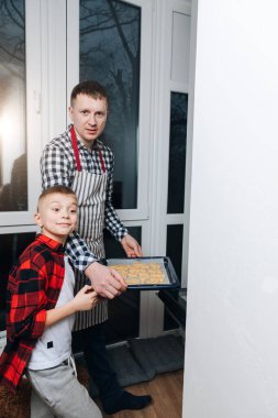 Bir çocuk ve babası fırına içinde Noel kurabiyeleri olan bir yemek tepsisi koyar. Noel için hazırlanıyorum. Evde kurabiye pişirmek. Ön görünüm