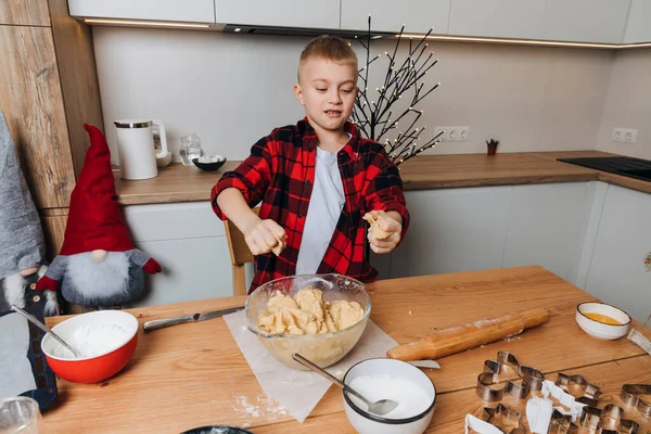 A boy make cookie dough at a wooden table in the kitchen. Cooking desserts at home. Joint activities with children. Front view
