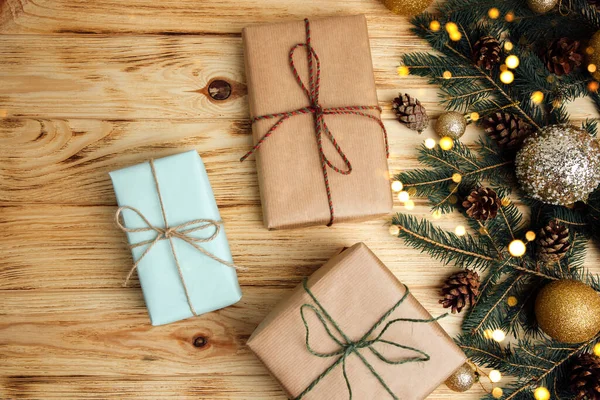 Noel arkaplanı selamlama içindir. Kahverengi kağıda sarılı hediyeler kozalaklı ağaç dalları, Noel oyuncakları ve açık ahşap arka planda kuru kozalaklar. Üst görünüm