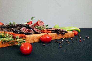 Yeşil kağıt ve domatesli ahşap tepside farklı tip ve boyutlarda sosisler. Koyu ahşap arka planda tütsülenmiş sosis seti. Ön görünüm