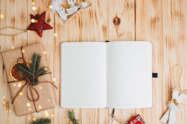 Noel arkaplanı selamlama içindir. Yeşil kozalaklı ağaç dalları, Noel oyuncakları ve açık ahşap bir arka planda açık bir defter. Üst görünüm