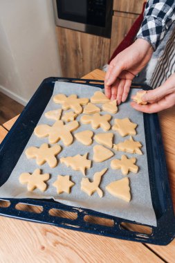 Erkek eli kapalı, şekillendirilmiş kurabiyeleri insan şeklinde serer. Yıldızlar, Noel ağaçları mutfaktaki ahşap bir masanın tepsisinde. Evde yemek pişirme tatlısı. Üst görünüm