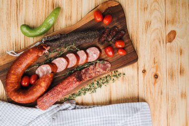 Farklı türde sosisler ve boyutlarda domatesli ahşap tepside. Ahşap arka planda tütsülenmiş sosis seti. Üst görünüm