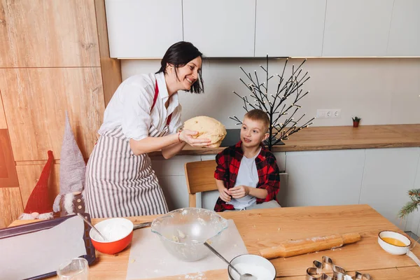 Mom and son are preparing dough for cookies at a wooden table in the kitchen. Cooking desserts at home. Joint activities with children. Front view